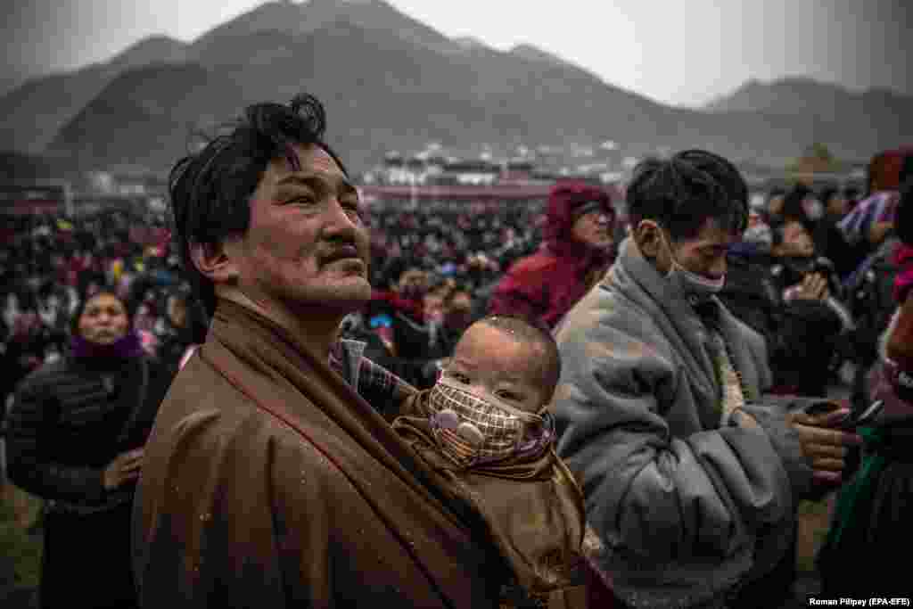 An ethnic Tibetan man holding a child looks at a huge sacred painting on cloth depicting Buddha during a prayer festival at Labrang Monastery in Xiahe, Gansu Province. (epa-EFE/Roman Pilipey)