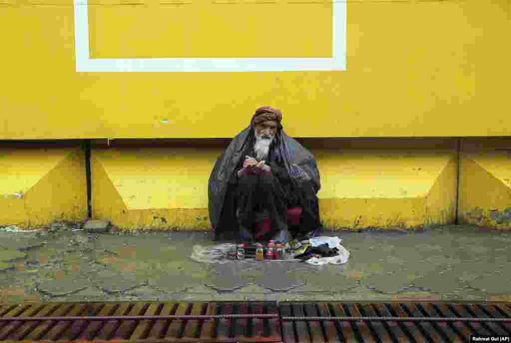 An Afghan shoeshiner covers himself with a plastic sheet in the rain as he waits for customers during quarantine in Kabul on April 28. (AP/Rahmat Gul)