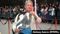 Булат Нусумбек, режиссер документального фильма о Шакене Айманове, идет по красной дорожке с плакатом своего фильма. Алматы, 15 сентября 2014 года. 