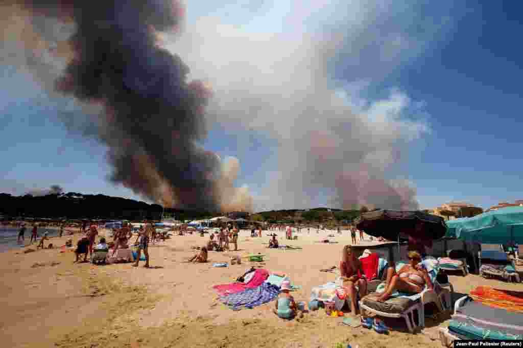 Smoke fills the sky above a burning hillside as tourists relax on the beach in Bormes-les-Mimosas, France, on July 26. (Reuters/Jean-Paul Pelissier)