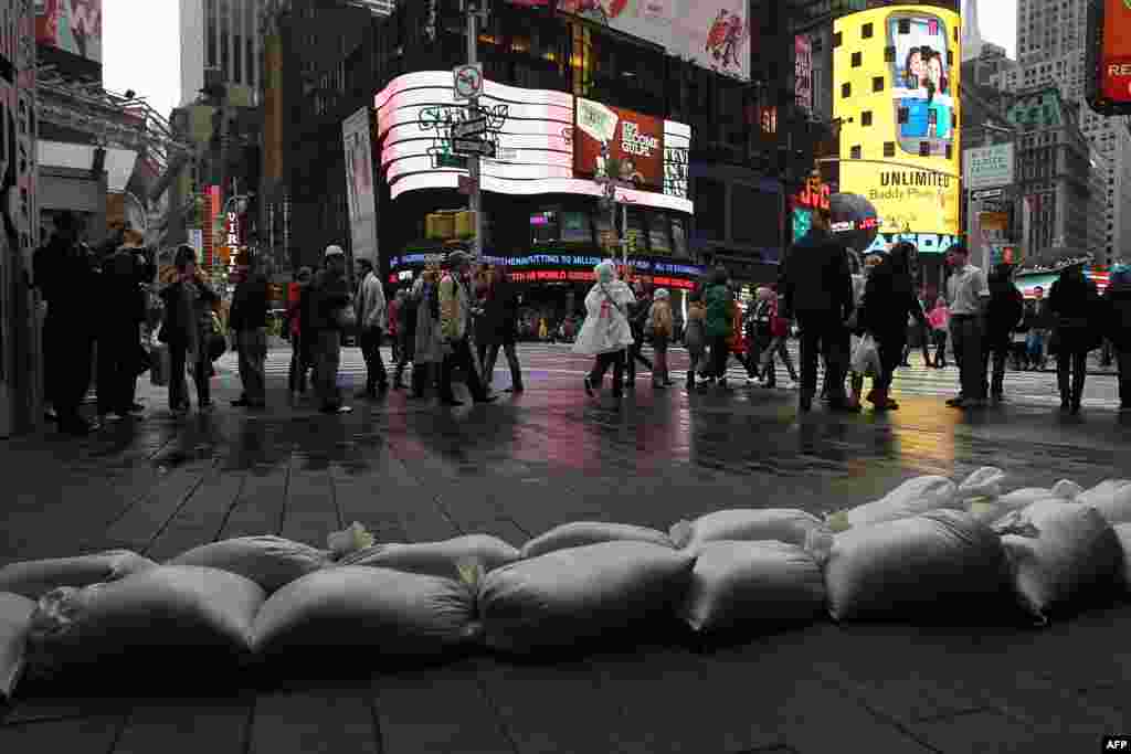 People walk by sand bags in front of a building in Times Square as Hurricane Sandy begins to affect the area in New York City. 