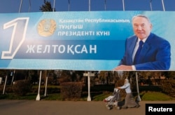 Қазақстан президенті Нұрсұлтан Назарбаевтың суреті бар үлкен баннердің жанынан өтіп бара жатқан әйел. Алматы, 30 қараша 2015 жыл.