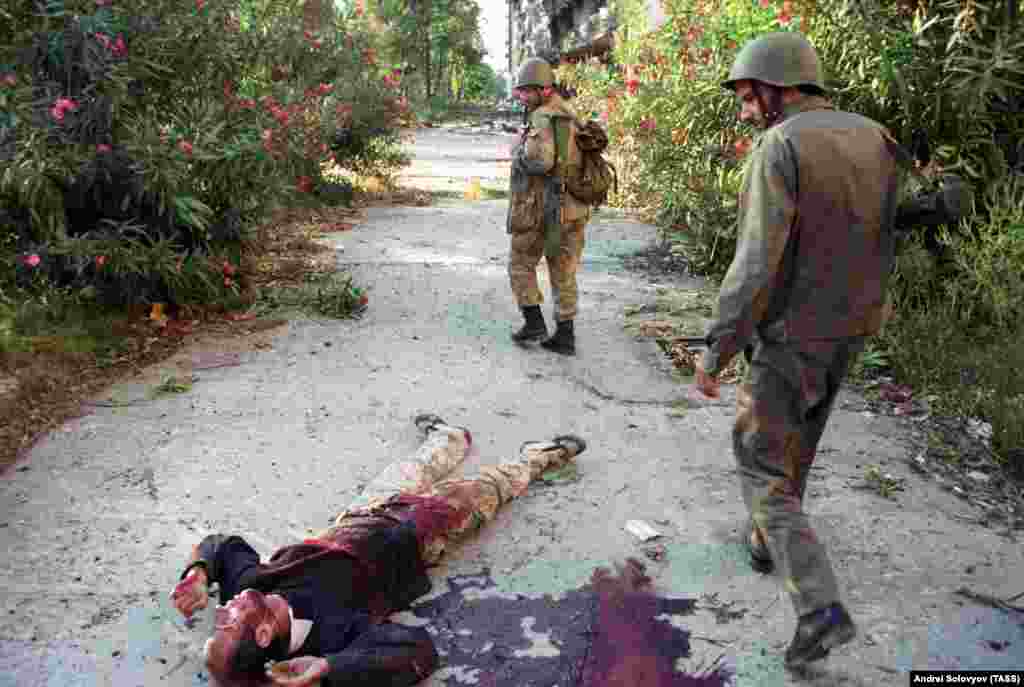 Unidentified fighters walk by a casualty of house-to-house fighting in Sukhumi. While the Abkhaz were strengthened by Russian troops and a motley array of &quot;mountain people,&quot; the Georgian side was bolstered by &quot;emptying the jails.&quot; According to a Human Rights Watch report, Georgian criminals were released from prison in return for joining the fight in Abkhazia.