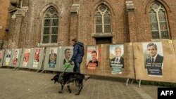 11 kandidatyň kampaniýa plakatlarynyň ýanyndan geçip barýan adam, Caestre, 21-nji aprel, 2017