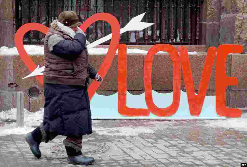 An elderly woman shivers with cold as she passes a decoration in the shape of a heart and the letters &quot;Love&quot; on Valentine&#39;s Day in Kyiv on February 14. (AFP/Serhey Supinsky)