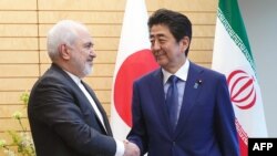 Iranian Foreign Minister Mohammad Javad Zarif (L) and Japanese Prime Minister Shinzo Abe shake hands at Abe's official residence in Tokyo on May 16, 2019. 