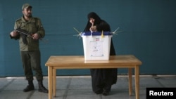 A woman from the Iranian city of Qom casts her vote in parliamentary elections on March 2 as a policeman stands guard.