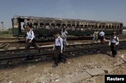 FILE: Students walk past the doused car of a train which caught fire as they head home along a railway track at Cantonment railway station in Karachi.