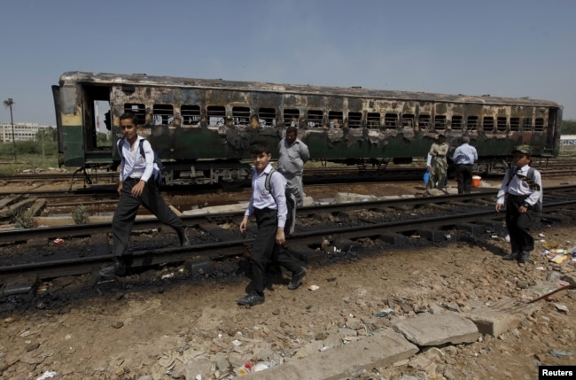 Fearing Debt Trap Pakistan Rethinks Chinese Silk Road Projects - file students walk past the doused car of a train which caught fire as they