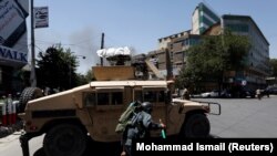 An Afghan policeman covers himself as smoke rises from the site of an attack in Kabul on July 31.