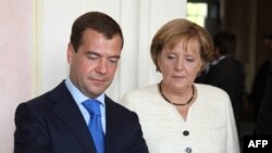 Russian President Dmitry Medvedev (left) signs a guest book during a meeting with German Chancellor Angela Merkel in Munich on July 16.