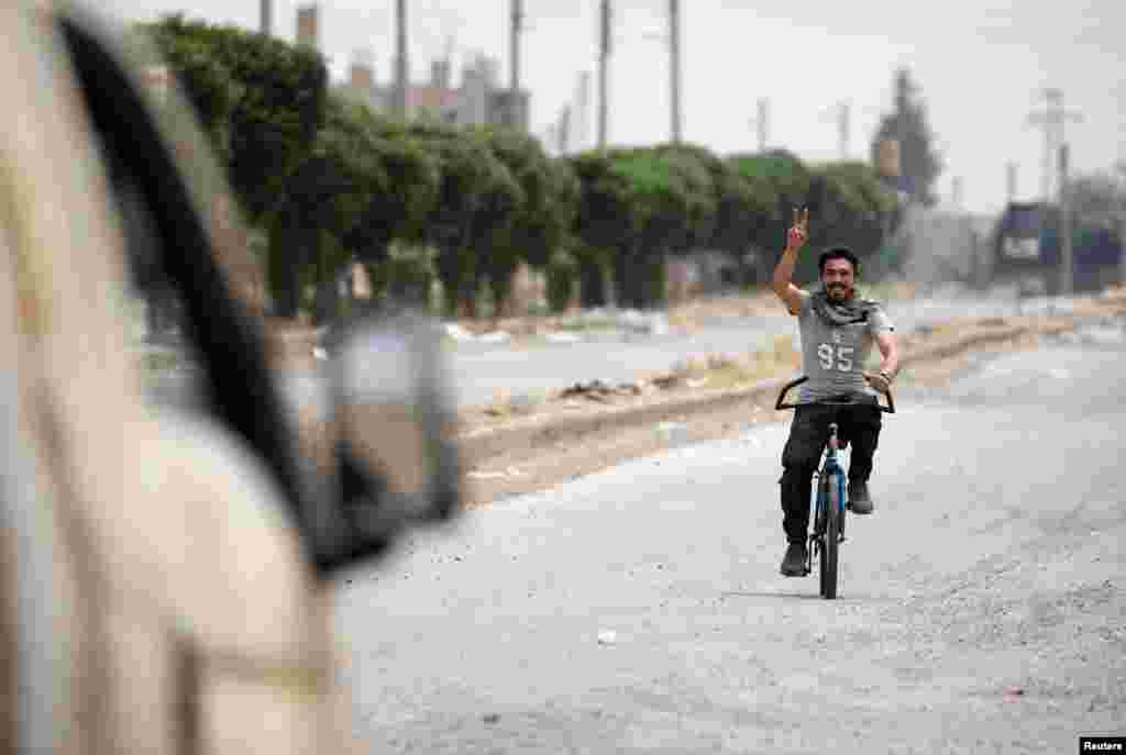 Syria -- A civilian riding a bicycle gestures towards a vehicle of the Syrian Democratic Forces (SDF) fighters in the Raqqa's al-Sanaa industrial neighbourhood, June 14, 2017