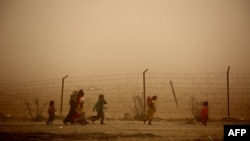 Syrian children walk around the camp grounds during a sandstorm at a temporary refugee camp in the village of Ayn Issa, housing people who fled the Islamic State group's Syrian stronghold of Raqqa.