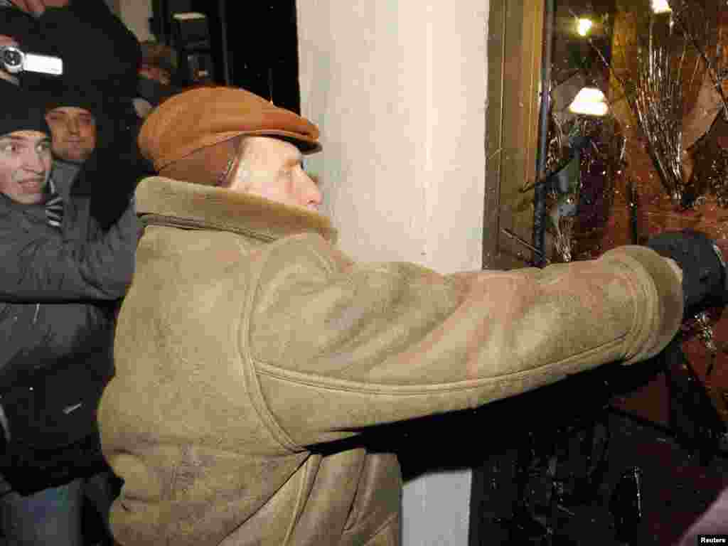 Një burrë nga radhët e grupit të protestuesve në përpjekje për të thyer derën e godinës së Parlamentit. 