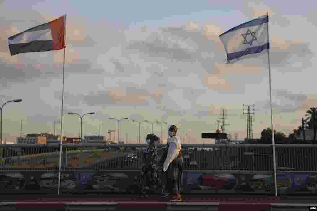 Women wearing face masks against the coronavirus walk past United Arab Emirates and Israeli flags at the Peace Bridge in Netanya, Israel, Sunday, Aug. 16, 2020. 