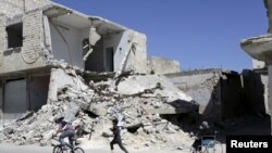 Syria -- A woman sits on a wheelchair near a damaged building, as a boy follows another one riding a bicycle in the rebel-controlled area of Maaret al-Numan town in Idlib province, April 1, 2016