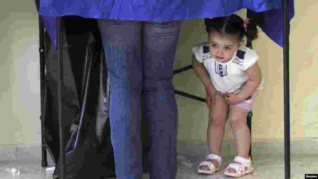 A girl peers under a polling booth while her mother prepares to vote at a polling station in Athens during Greece's general elections on May 6. (Reuters/Panayiotis Tzamaros)