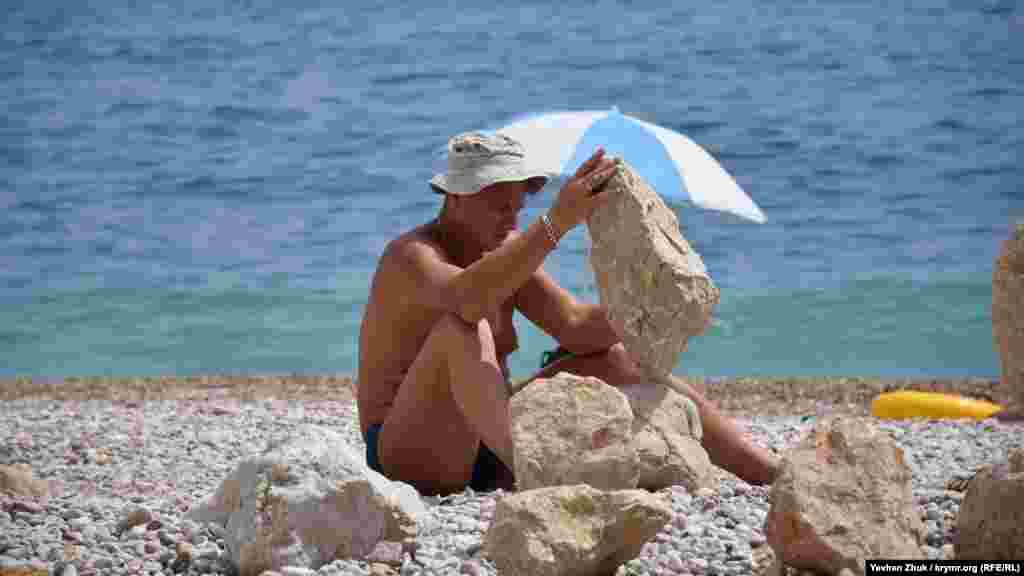 Мужчина устанавливает тяжелые камни один на другой на пляже &laquo;Васили&raquo; близ Балаклавы. Это называется балансировкой камней