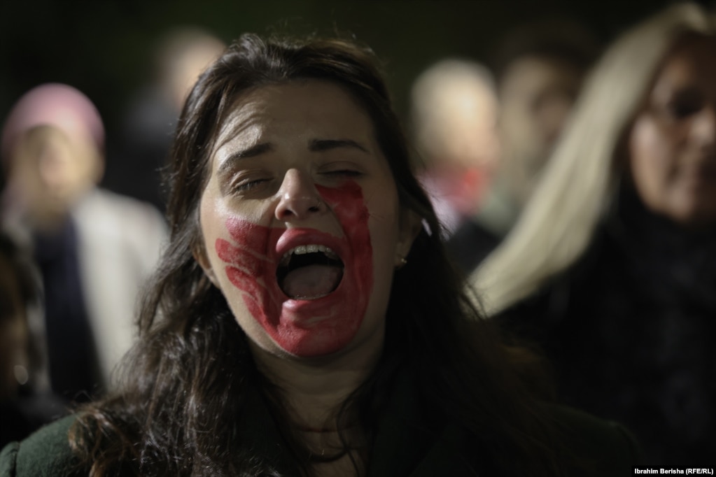 Një grua me gojën e ngjyrosur me të kuqe merr pjesë në marshin për të kërkuar përgjegjësi institucionale për Arlinda Zekajn.Arlinda Zekaj kishte kërkuar vazhdimisht ndihmë nga institucionet e drejtësisë dhe sigurisë duke raportuar dhunë në familje, përfshirë edhe disa orë para se të vritej.
