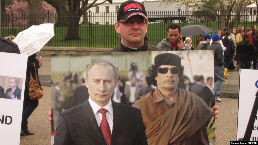 A protester holds up a photo of Vladimir Putin and Muammar Qaddafi in front of the White House on March 31, 2011.