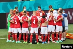  Съотборниците на Ериксен го обкръжават, до момента в който медицинският екип му прави сърдечен масаж, 12 юни 2021 година 