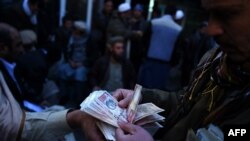 FILE: Afghan money changers count banknotes at the currency exchange Sarayee Shahzada market in Kabul.