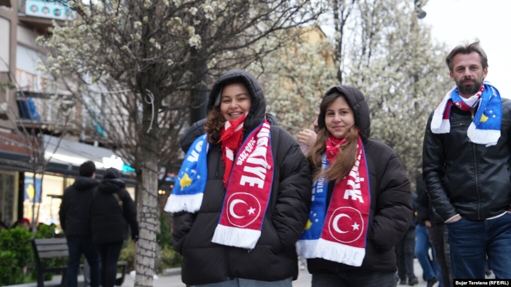 Një burrë dhe dy gra me shalle mbi supe të cilat mbajnë si emrin e Kosovës, ashtu edhe atë të Turqisë, pak para ndeshjes vendimtare mes Kosovës dhe Turqisë për një vend në Kupën e Botës 2026, të martën në Stadiumin "Fadil Vokrri".