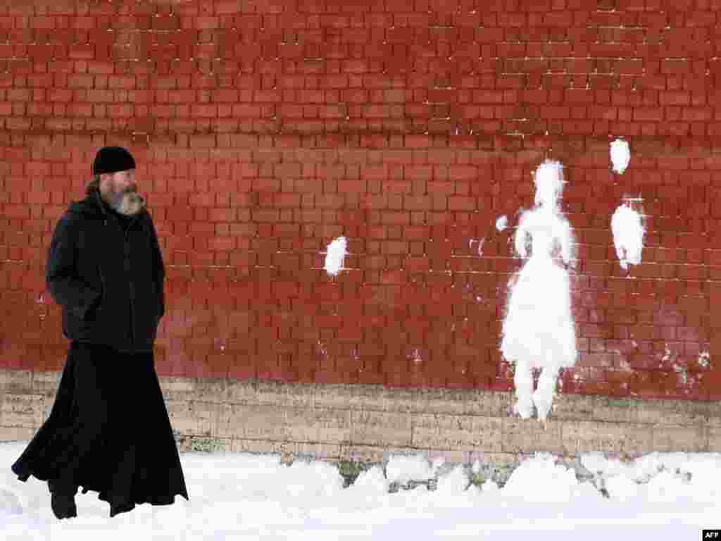 A Russian Orthodox priest looks at a silhouette made of snow on the wall of the St. Peter and Paul fortress in central St. Petersburg on January 20. Photo by Kirill Kudryavtsev for AFP