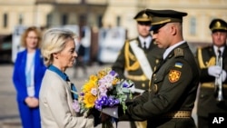 Presidentes së Komisionit Evropian, Ursula von der Leyen, (majtas) i dhurohet një buqetë me lule për ta vendosur në një mur në Kiev që përkujton ushtarët e rënë ukrainas në luftën me Rusinë, më 20 shtator.