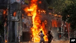 Protestuesit vrapojnë pranë një dyqani të përfshirë nga zjarri gjatë protestave antiqeveritare në Bangladesh, 4 gusht 2024.