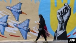 Жанчына крочыць узбоч мілітарысцкага мурала ў Тэгеране 8 красавіка