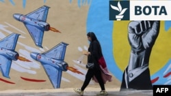 Një grua duke kaluar pranë një murali me mesazhe kundër SHBA-së dhe Izraelit në Teheran më 8 prill. 