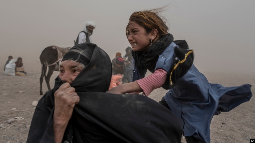 A frightened Afghan girl and woman receive aid on October 12 while enduring a fierce sandstorm after the earthquake in the Zenda Jan district of Herat Province.