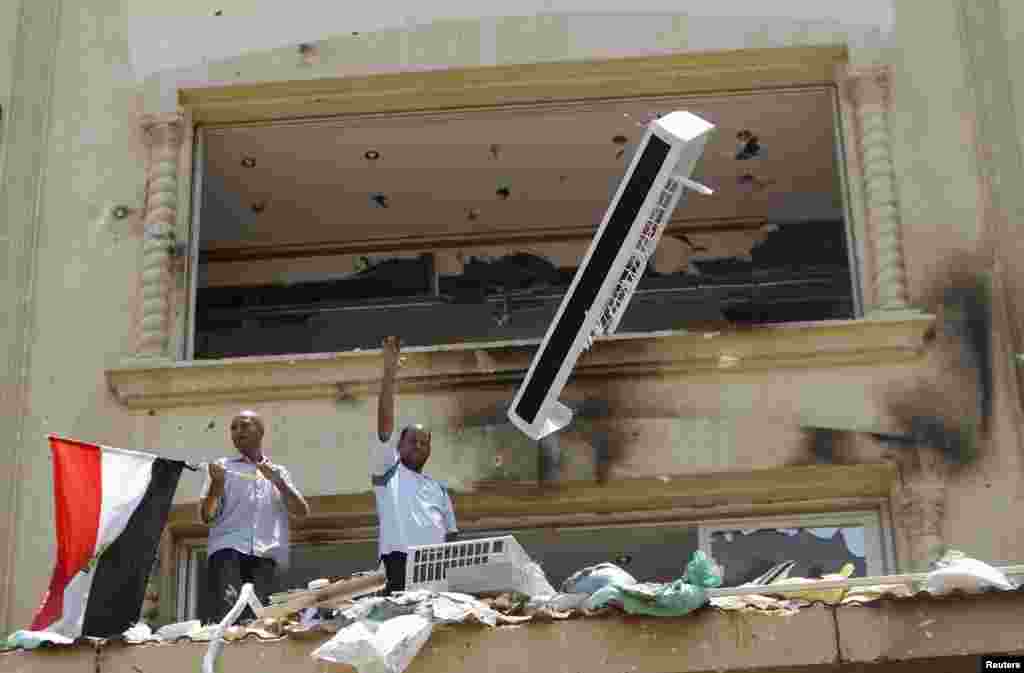 A looter gestures as part of an air-conditioner is thrown down from the Muslim Brotherhood offices.