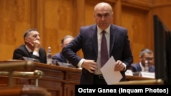 Premierul Ilie Bolojan se pregătește să citească unul dintre cele cinci discursuri pentru proiectele prin care guvernul și-a asumat răspunderea în Parlament. 