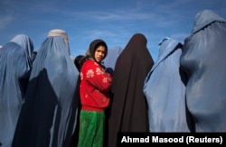 An Afghan girl stands among widows clad in burqas.