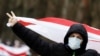 A man carrying a former white-red-white flag of Belarus shows a V-sign during opposition protests in Minsk on December 13. (AFP)