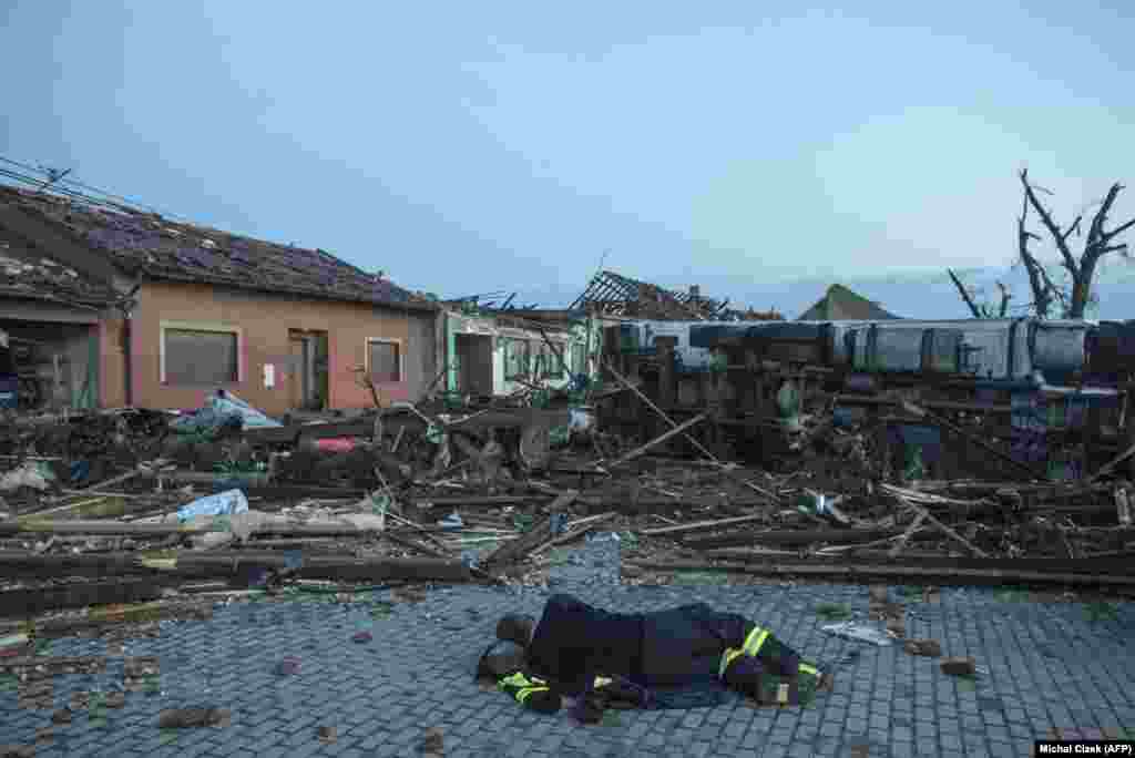 Пожежник відпочиває на вулиці рано вранці 25 червня 2021 року перед пошкодженими будівлями та транспортним засобом у селі Моравська Нова Вес &nbsp;