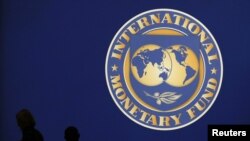 Japan -- Visitors are silhouetted against the logo of the International Monetary Fund at the main venue for the IMF and World Bank annual meeting in Tokyo, 10Oct2012