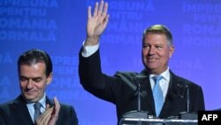 Romanian President Klaus Iohannis (right) with Prime Minister Ludovic Orban by his side waves to supporters after the first-round results are announced. 