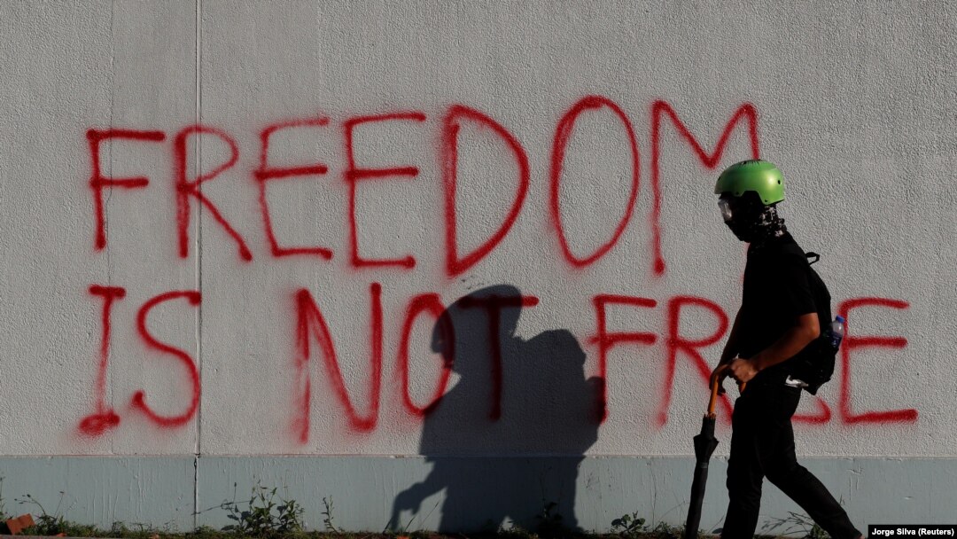 Un protestatar antiguvernamental din Hong Kong trece prin dreptul unui graffitti în timpul protestului din cartierul Sha Tin, care are loc de Ziua Națională a Chinei