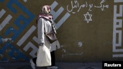 A woman walks past writing on a wall in Persian that says "Down with Israel" in northern Tehran.