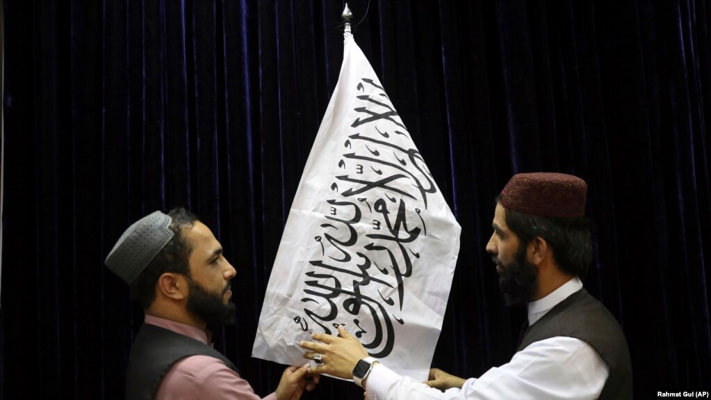 دو نفر از طالبان قبل از کنفرانس مطبوعاتی سخنگوی طالبان پرچم خود را نصب می‌کنند، کابل، ۱۷ اوت ۲۰۲۱