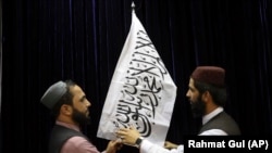 Talibanski zvaničnici postavljaju zastavu talibana pre početka konferencije za novinare 17. avgusta na kojoj su pokušali da ublaže strahve da će ponovo vratiti represivan režim kao kada su prethodno kontrolisali Avganistan od 1996. do 2001.