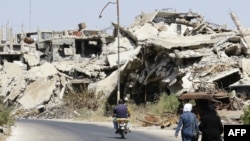 Syrians walk and drive past destroyed buildings in the government held Jouret al-Shiah neighborhood of the central Syrian city of Homs, September 19, 2016