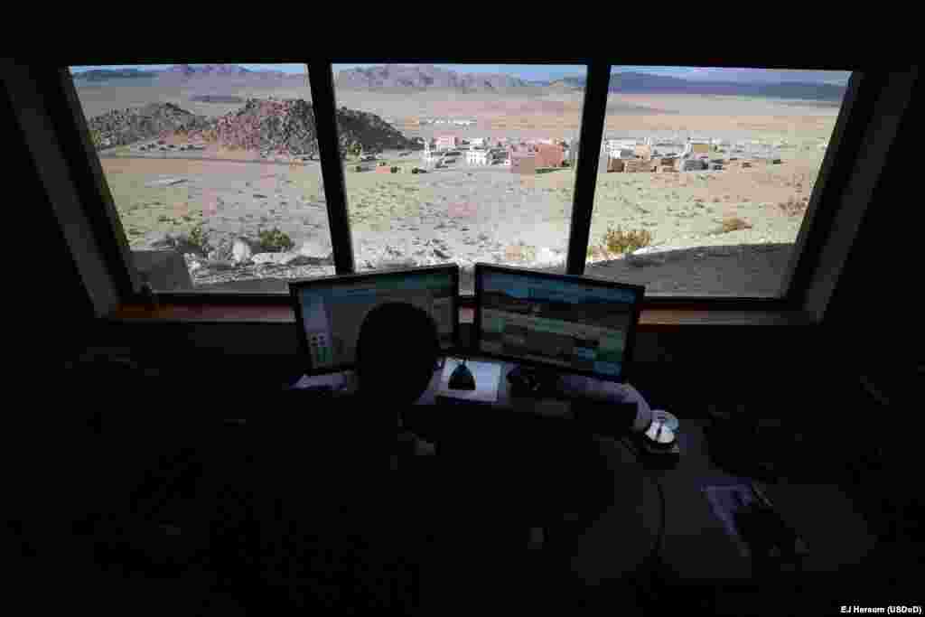 A computer operator watches screens displaying live interior and exterior images of the village.