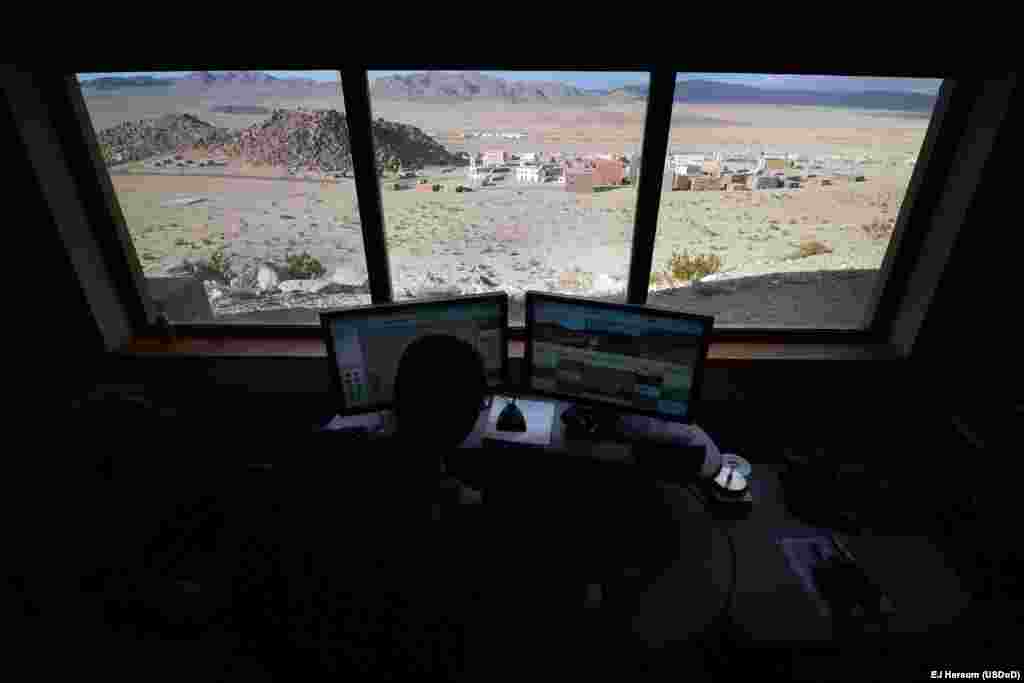 A computer operator watches screens displaying live interior and exterior images of the village. 