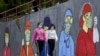 Девојки со заштитни маски поминуваат покрај мурал инспириран од Ковид 19 во Скопје. 