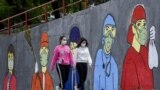 MACEDONIA - Two young women walk by a mural inspired by the "Covid19" (novel coronavirus) in Skopje on May 7, 2020