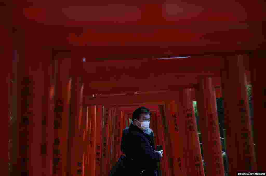 Мужчина в защитной маске проходит через красные деревянные ворота в храме Незу в Токио, Япония. 5 марта 2020 года.